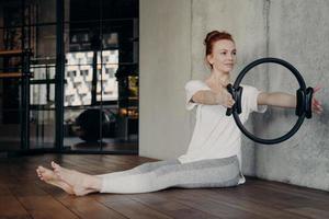 Young focused redhead woman doing strength exercises with pilates ring photo