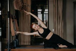 bella mujer haciendo ejercicio y estirándose en cadillac reformer foto