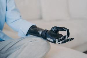 Cyber hand of disabled person which is sitting in lotus pose on couch. Robotic arm in meditation. photo