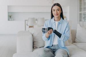 Positive disabled young woman is disassembling bionic arm prosthesis and smiling. photo