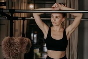 Hermosa mujer joven en pose de ocio inclinándose hacia adelante en el marco de la máquina de pilates foto