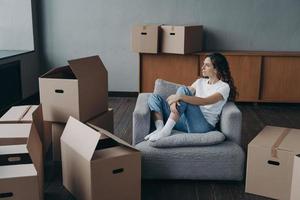 Happy woman is an apartment buyer. Mover is dreaming among boxes in living room of new home. photo