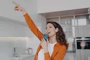 Favourite song karaoke singing at home. Happy caucasian woman in airpods relaxing and dancing. photo