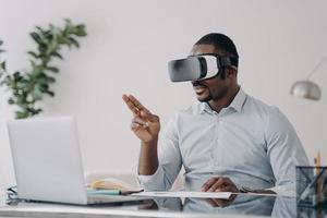 African businessman wearing vr glasses works at laptop manages business project in virtual reality photo