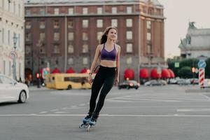 una foto completa de una mujer delgada y deportiva en paseos activos en cuchillas disfruta de la actividad física al aire libre durante las poses de los cálidos días de verano en un lugar urbano sobre asfalto. concepto de patinaje y ocio