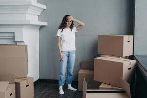 Tired girl is moving. Woman getting headache from boxes packing and going to relocate. photo