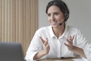 Pleasant young Italian female director wearing wireless headphones, looking at laptop screen photo