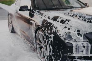 Washing off white soap foam from car with high pressure washer outdoors photo