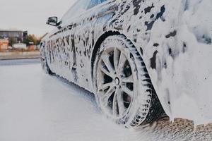Vehicle in white soapy foam during regular car wash outdoors, auto getting wash with soap photo