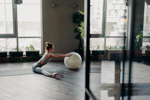 Sportive woman stretching legs in split position, training with large exercise ball photo