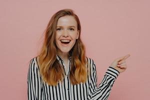 Laughing young female pointing aside at copy space for advertisement with forefinger photo