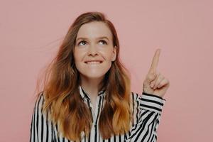 Young woman thinking while biting lips and having pointer finger up photo