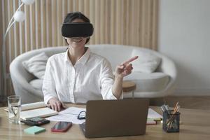 Female office worker in vr headset or virtual reality goggles touching objects in cyberspace photo