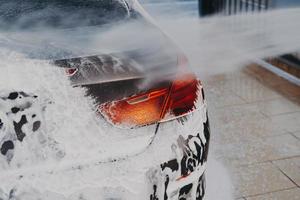 Washing car exterior surface with high pressure washer at self-serve cleaning station outdoors photo