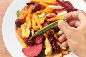 Mixed healthy vegetable chips with okra, carrots, pumpkin, beetroot and shiitake mushrooms and man's hand. photo