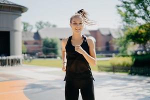 feliz y enérgica deportista corre en el estadio tiene cola de caballo flotando en el viento vestida con ropa deportiva siendo corredor activo tiene una sonrisa positiva disfruta de los entrenamientos matutinos regulares te motiva para el deporte foto