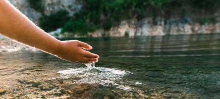 la mano toca el agua en el estanque con sol foto