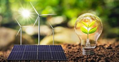 concepto de energía limpia y ahorro de energía en la naturaleza. panel solar con aerogenerador. pequeño árbol y bombilla foto