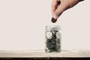 joven sosteniendo monedas poniendo en el vaso de la botella. concepto de ahorro de dinero o ahorro de impuestos para contabilidad financiera y negocios. foto