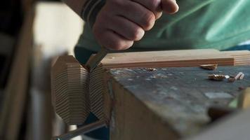 un carpintero corta un perfil de una pierna de madera con un cincel