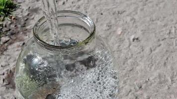 verser de l'eau propre dans un bocal en verre en gros plan sur un fond de béton.