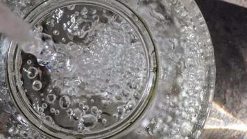 Wasser in ein Glasgefäß gießen. Spritzer und Blasen. Sicht von oben. video