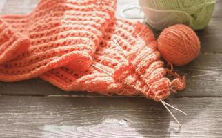 agujas de tejer, hilo naranja y tejido de punto texturizado en curso. foto