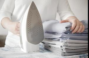 woman holding pile of bed clothes or bed linen and iron. home work concept. photo