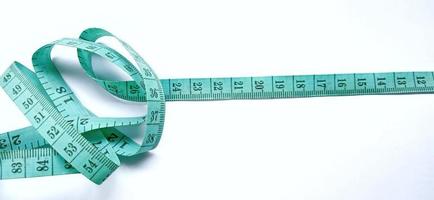 Old wrinkled green rubber tape measure with negative space. Rubber tape measure isolated on the gray white background. Useful for sewing cloth or fabric. photo