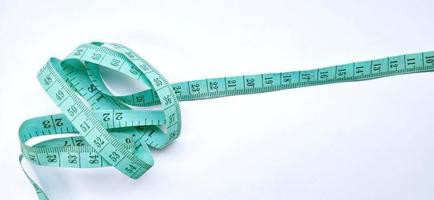 Old wrinkled green rubber tape measure with negative space. Rubber tape measure isolated on the gray white background. Useful for sewing cloth or fabric. photo