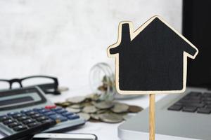 Wooden house model with blurred background of coins, calculator and notebook. photo