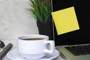 Sticky note on a notebook screen with other accessories and coffee on the table. photo