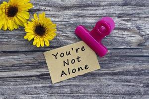 You are not alone text on torn paper with paper clip holder on wooden surface. photo