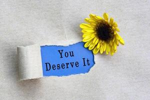 You deserve it text on torn hole in the sheet of brown paper on green background photo