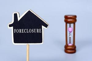 Foreclosure text on wooden house model with blurred hourglass background. photo