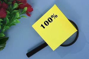 100 percent number on colorful note with artificial flower on wooden background. photo