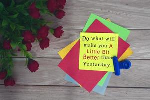 Motivational quote on colorful note with artificial flower on wooden background. photo