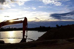 Excavators are stationary after work in the evening, using the arms of the car as a frame to see the beautiful sky and clouds of various colors in the evening, a beam of light into the beautiful river photo