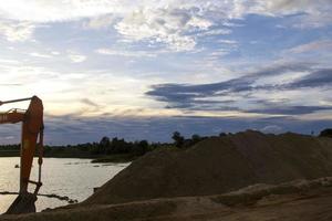 Excavators are stationary after work in the evening, using the arms of the car as a frame to see the beautiful sky and clouds of various colors in the evening, a beam of light into the beautiful river photo