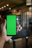 Joven mano usando un teléfono inteligente con pantalla verde en el café foto