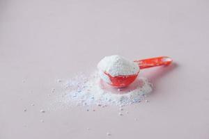 Washing powder in plastic spoon on blue background photo