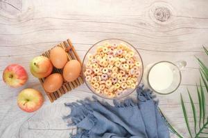 top view of colorful cereal corn flakes, apple , egg and milk on table photo