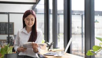 primer plano retrato de una hermosa joven asiática sonriendo y mirando un libro en el café foto