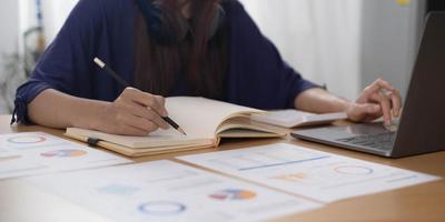 Cerca de la mano de la mujer o del contador que sostiene el lápiz que trabaja en la calculadora para calcular el informe de datos financieros, el documento de contabilidad y la computadora portátil en la oficina, concepto de negocio foto