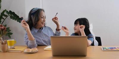 Asian grandmother and granddaughter happily pencil drawing at home photo