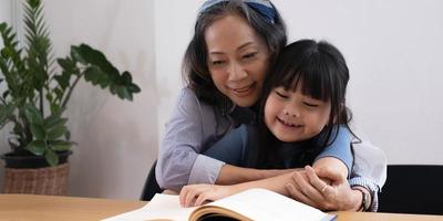 feliz abuela de familia asiática leyendo a su nieta un libro infantil en casa foto