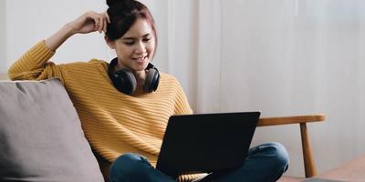 Cheerful freelancer working on laptop sitting on couch and listening to music in headphones, copyspace photo