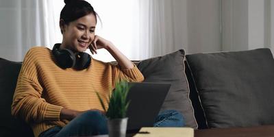alegre freelancer trabajando en una laptop sentada en el sofá y escuchando música en auriculares, copyspace foto