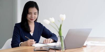 Happy young asian businesswoman sitting on her workplace in the office. Young woman working at laptop in the office. photo