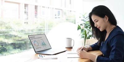 Beautiful Asian businesswoman analyzes charts using laptop calculator at the office. photo
